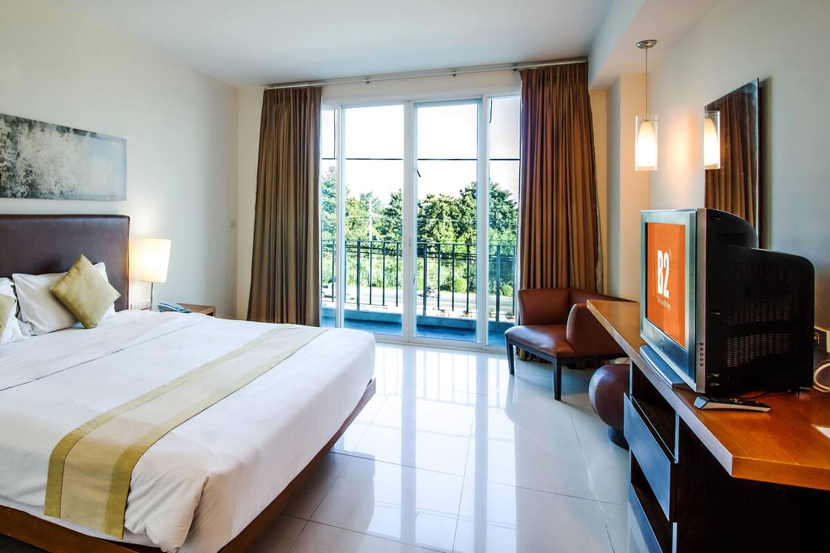 A hotel room with a large bed, a television, a desk, and a view of the outdoors.