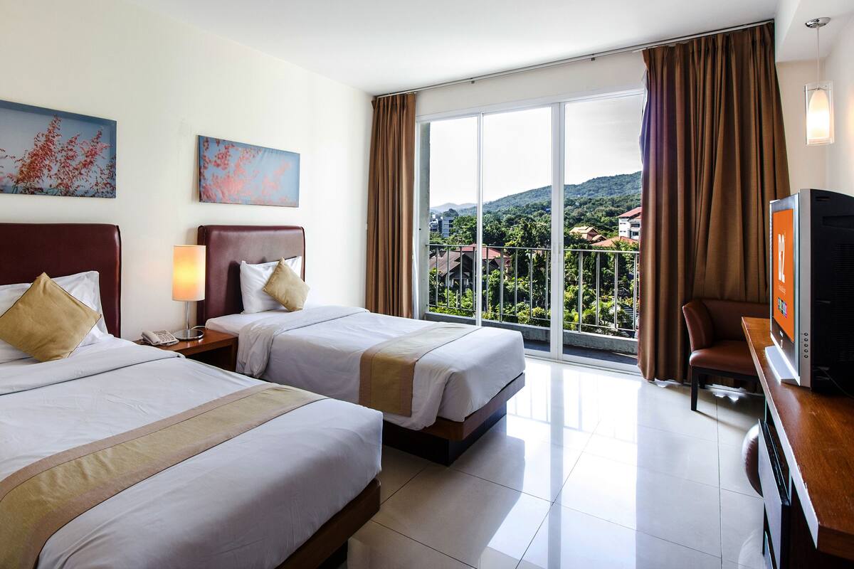 A hotel room with two beds, a TV, a balcony with a view of the mountains, and artwork on the walls.