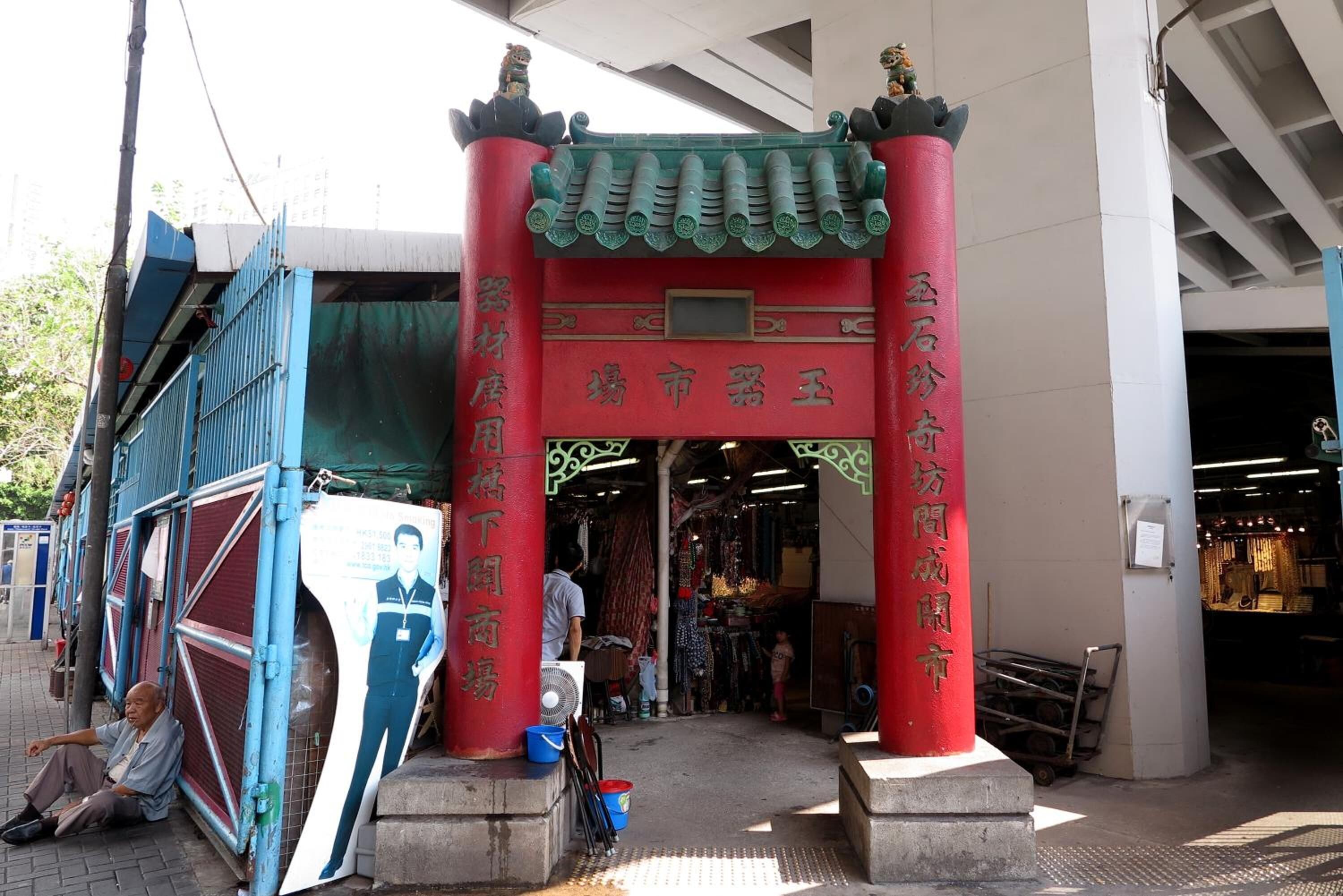 A traditional Chinese gate with red pillars and green roof, leading to a market area.