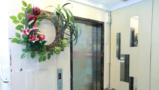 An elevator with a digital floor indicator, a trash bin, and decorative plants. - Shanghai Red (Kowloon)