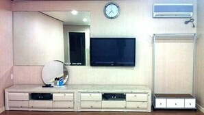 A room with a large mirror, a flat-screen TV mounted on the wall, a wooden cabinet with drawers, and an air conditioning unit. - Songnisan Grand Hotel & Condo (Boeun)
