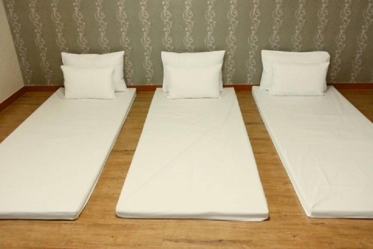 Trois lits simples avec du linge de lit blanc, dans une chambre dont les murs sont recouverts d’un papier peint à motifs.