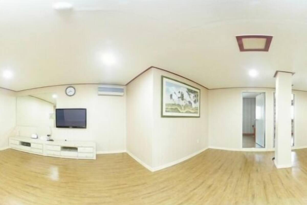 Une pièce spacieuse avec un plancher en bois, un téléviseur à écran plat fixé au mur, une armoire blanche et un tableau encadré.