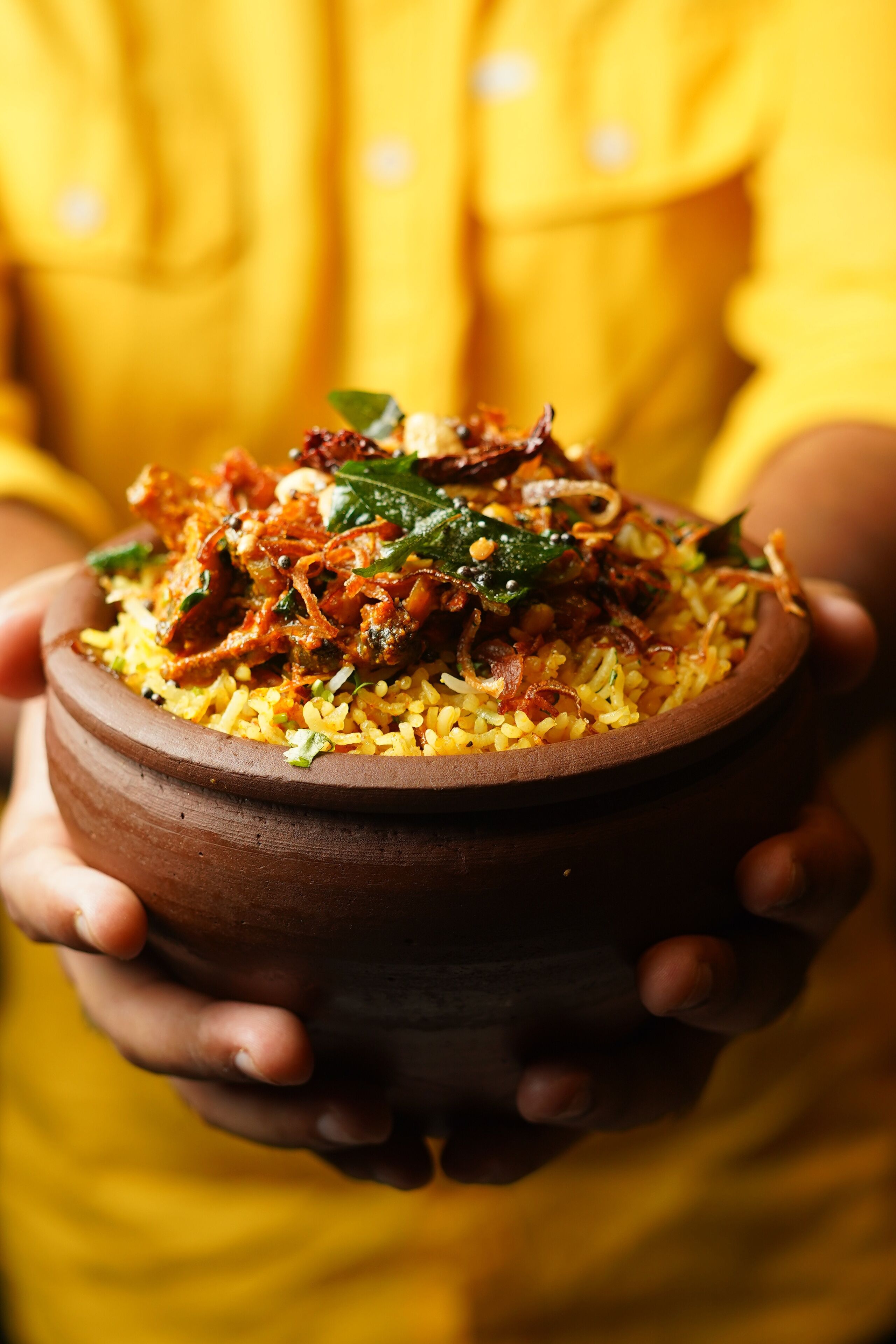 Una persona sosteniendo un tazón de arroz amarillo con verduras y especias.