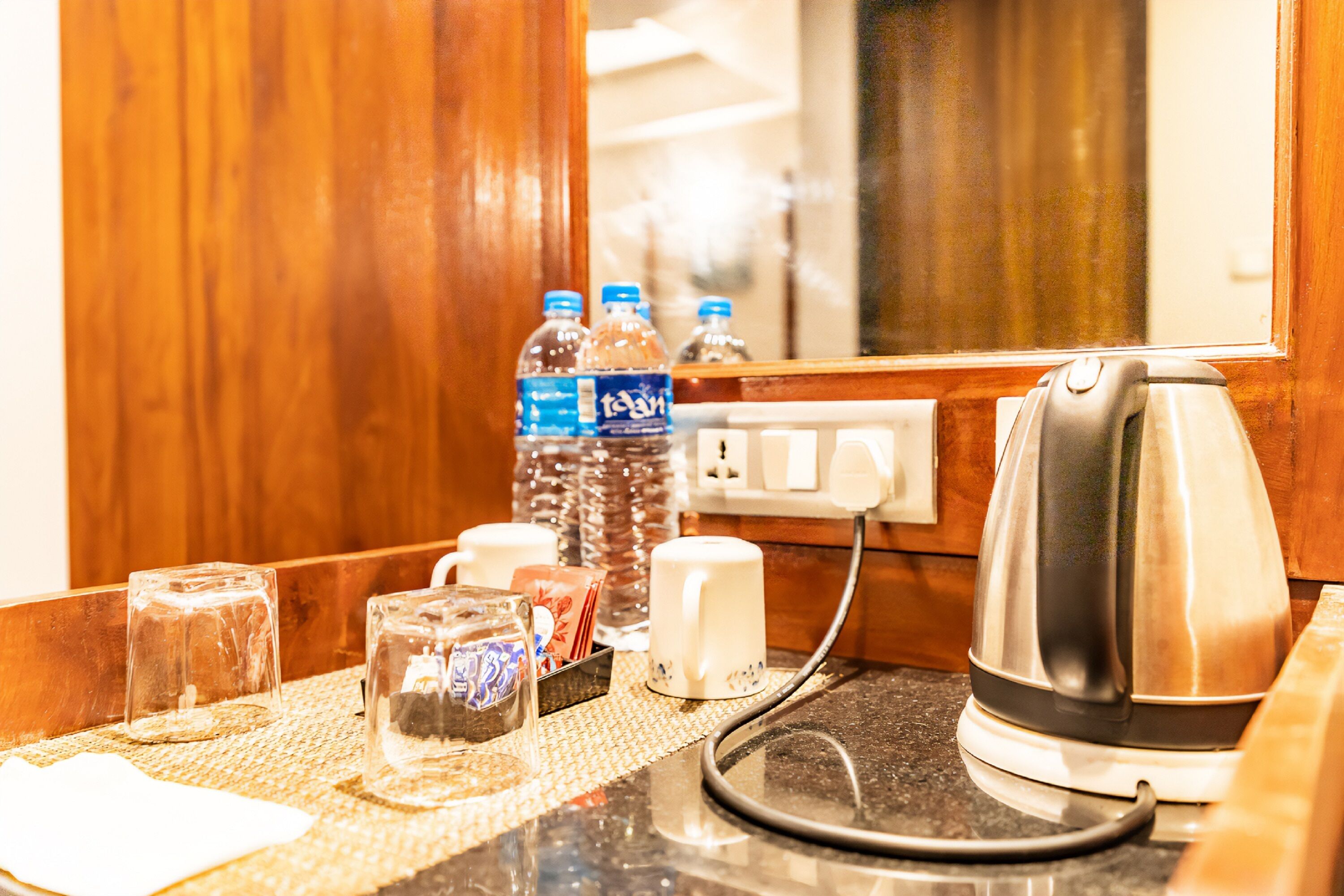 Mostrador de recepción de hotel con una tetera, botellas de agua, vasos y una caja de pañuelos.