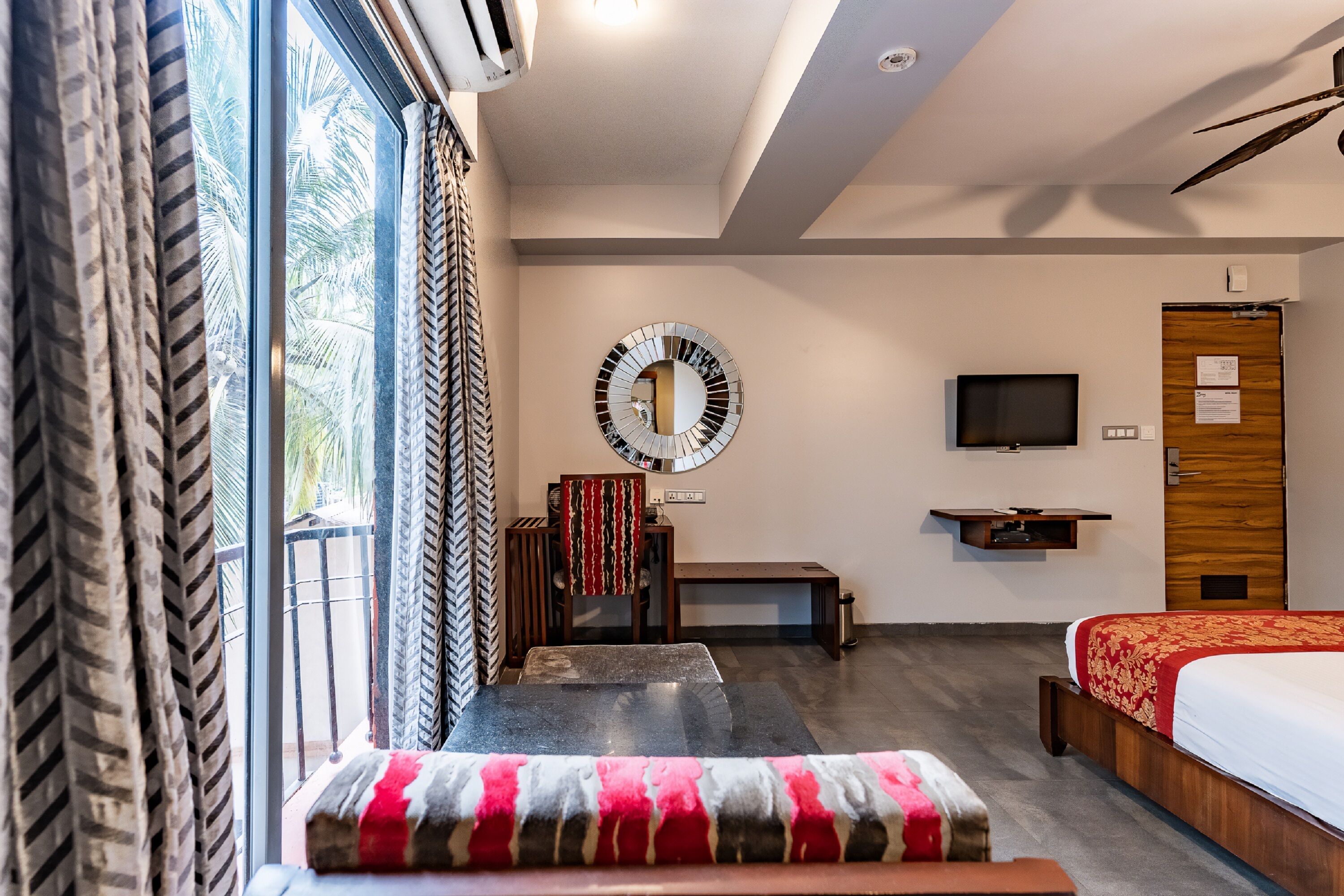 Habitación de hotel con cama, televisor, escritorio y un amplio ventanal con cortinas.