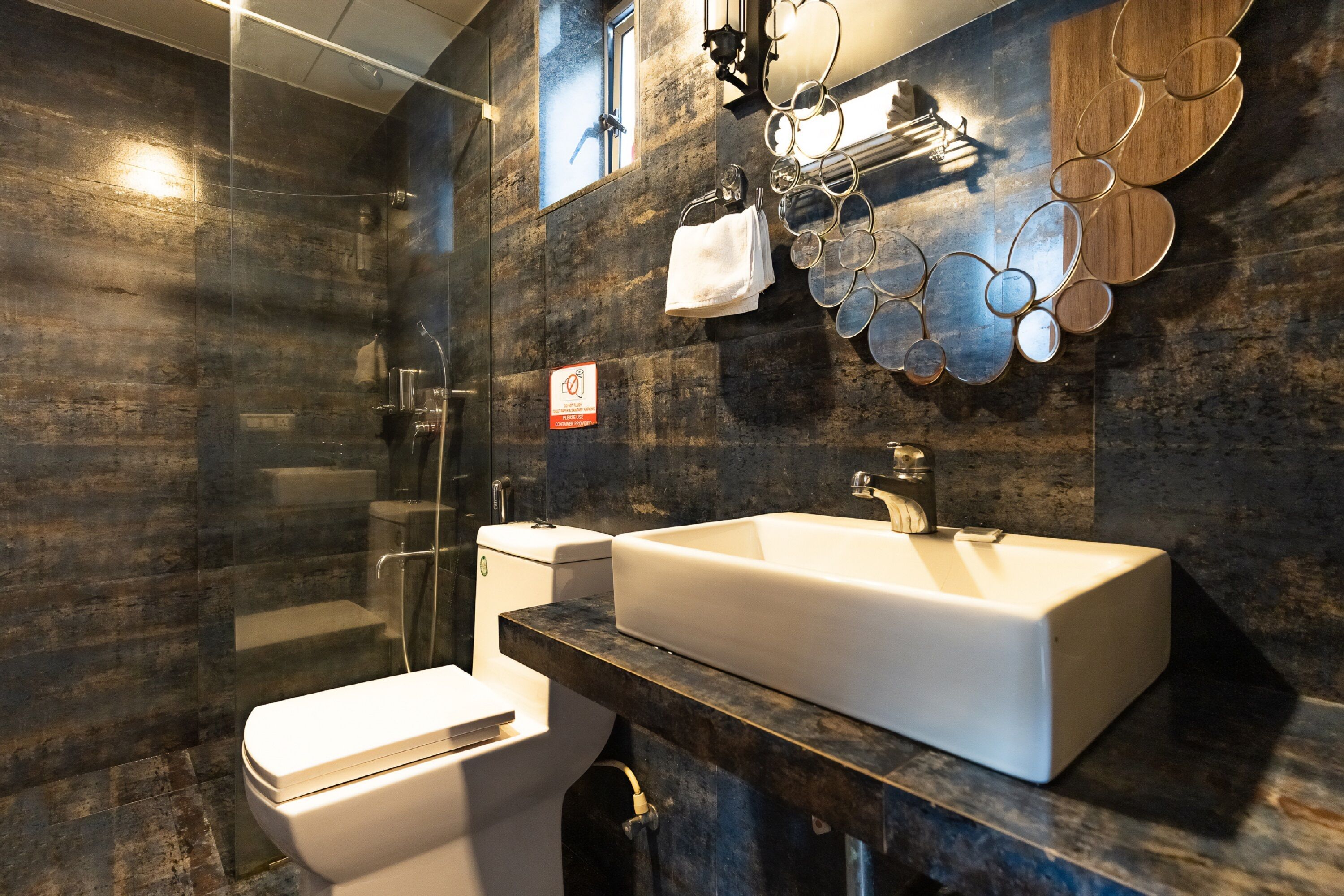 A modern bathroom with a glass shower enclosure, a white toilet, and a large white sink with a dark countertop.