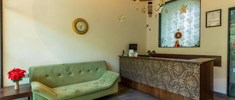 A reception area with a green sofa, a wooden reception desk, a clock, and a chandelier.