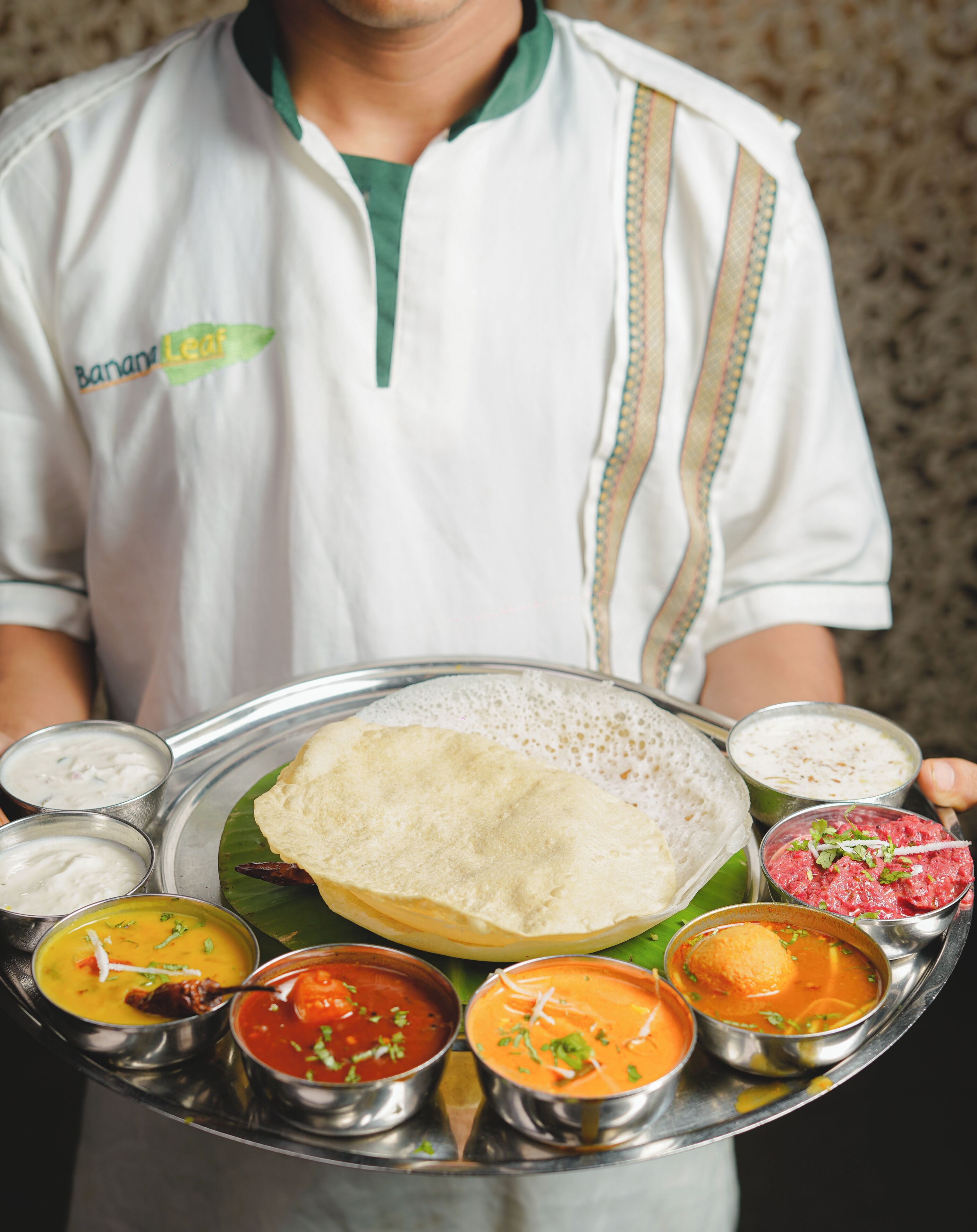 Una persona sirve una variedad de platos del sur de la India sobre una bandeja de metal.