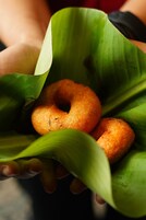 Una mano sostiene una hoja verde con dos rosquillas doradas y marrones.