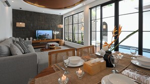 Uma sala de estar moderna com uma parede de pedra, uma televisão e um espaço de jantar com mesa, cadeiras e velas.