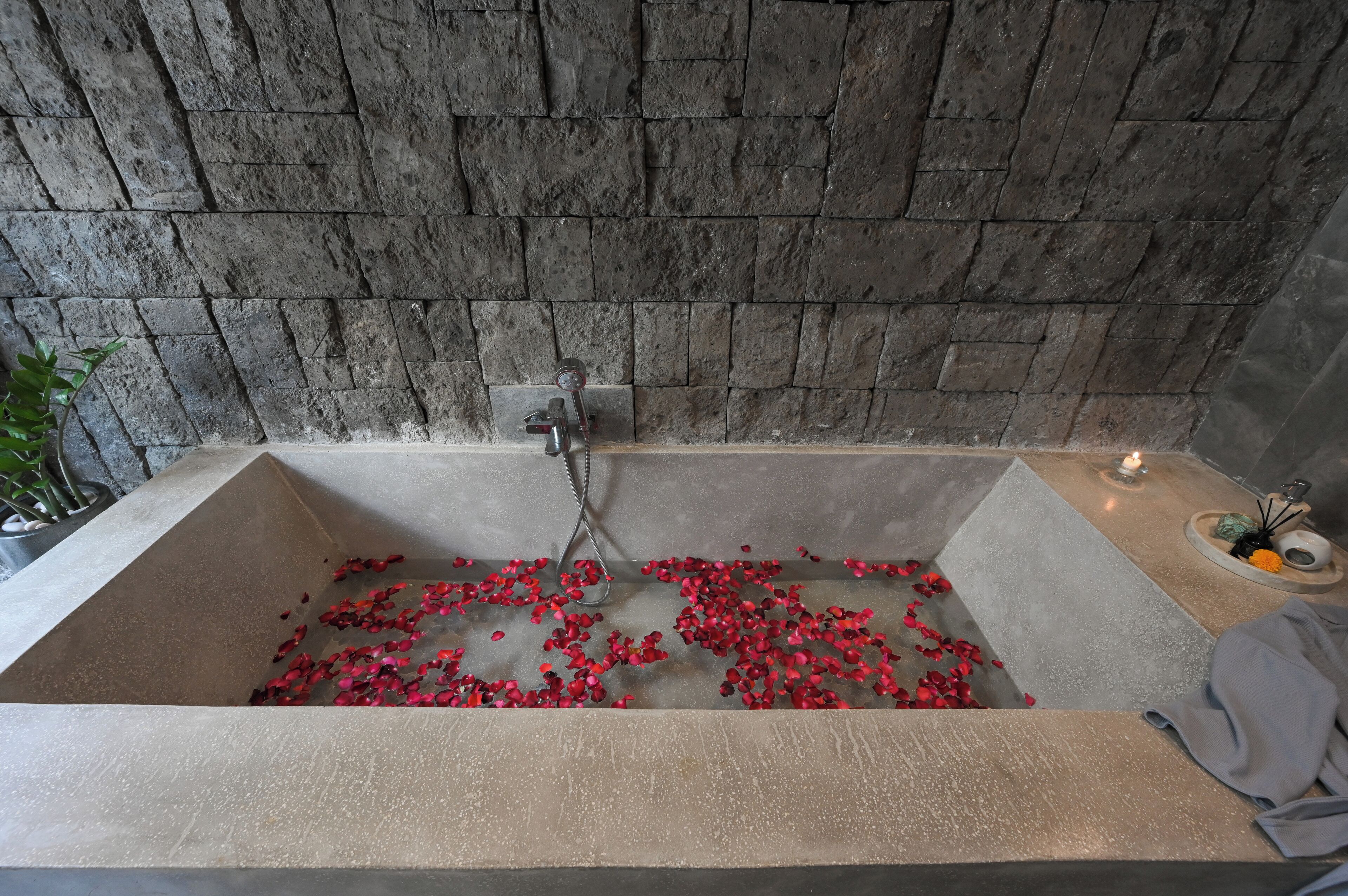 A bathtub with rose petals, a candle, and a towel on the side.