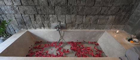 A bathtub with rose petals, a candle, and a towel on the side.
