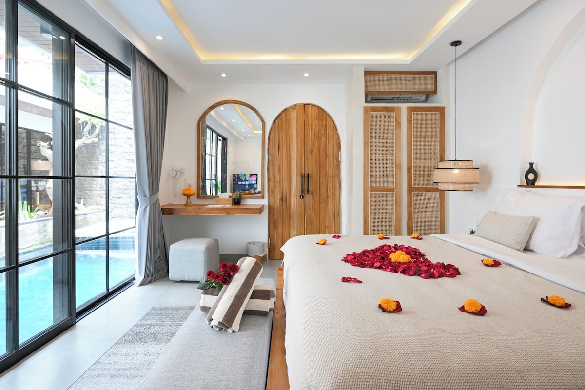 Een moderne hotelkamer met een groot bed, uitzicht op een zwembad, een houten garderobe en een spiegel.
