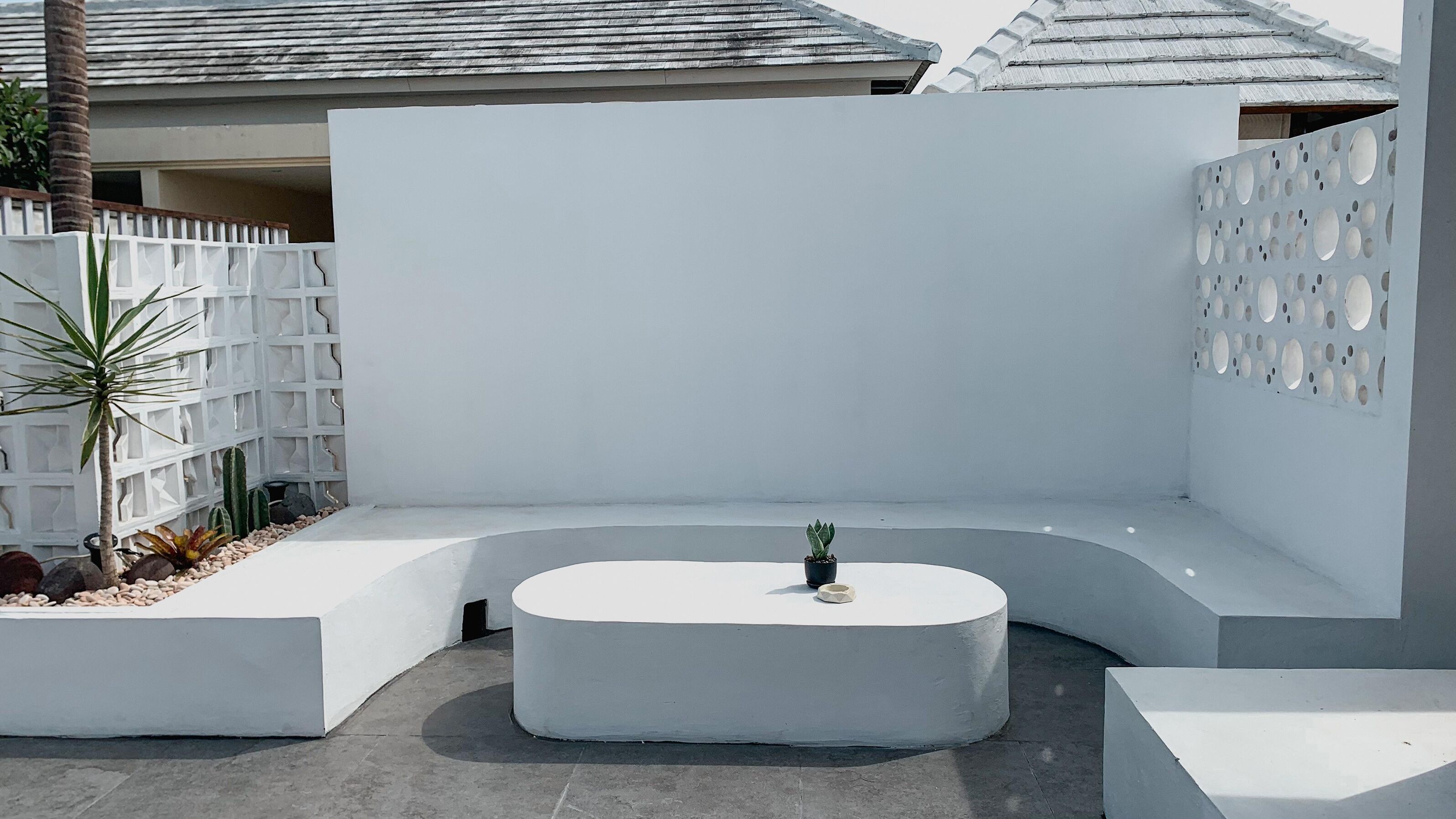 Un espace extérieur moderne, aménagé avec un banc blanc aux lignes courbes et une petite table agrémentée d’une plante en pot.