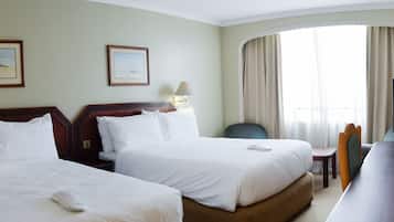 A hotel room with two beds, a desk with a television, and a large window with curtains.