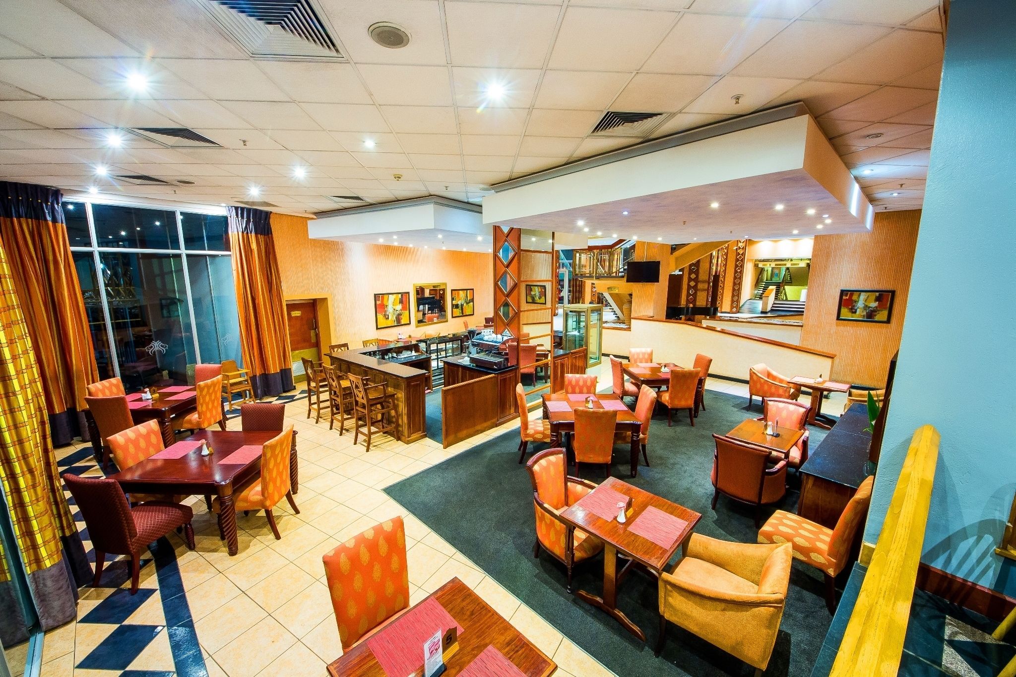 Un hall de hotel con varias zonas de comedor, un bar y una escalera que sube a un nivel superior.