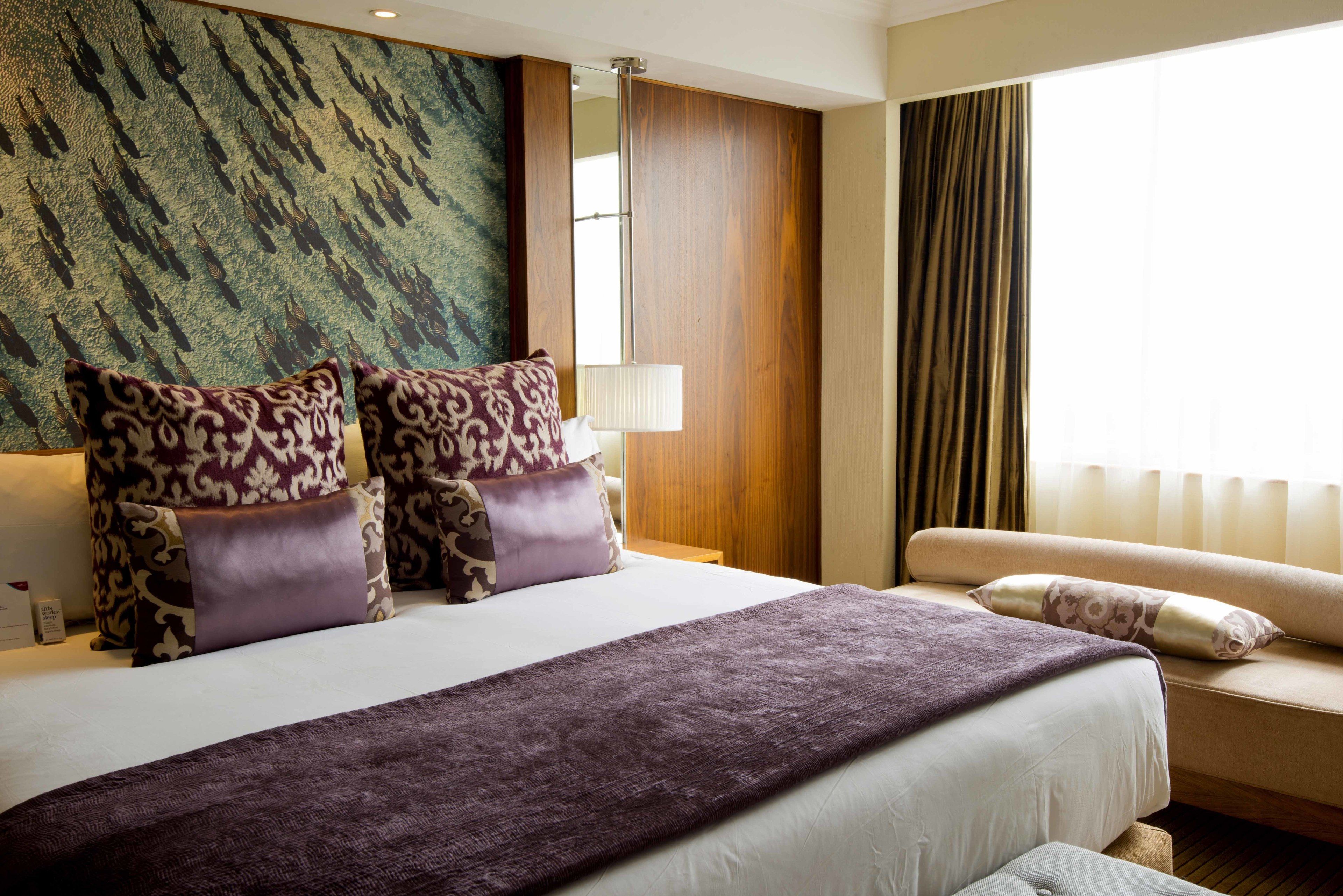 Une chambre d’hôtel avec un grand lit, deux tables de chevet, un canapé et une grande fenêtre avec des rideaux.