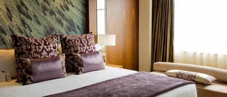 A hotel room with a large bed, two side tables, a sofa, and a large window with curtains.