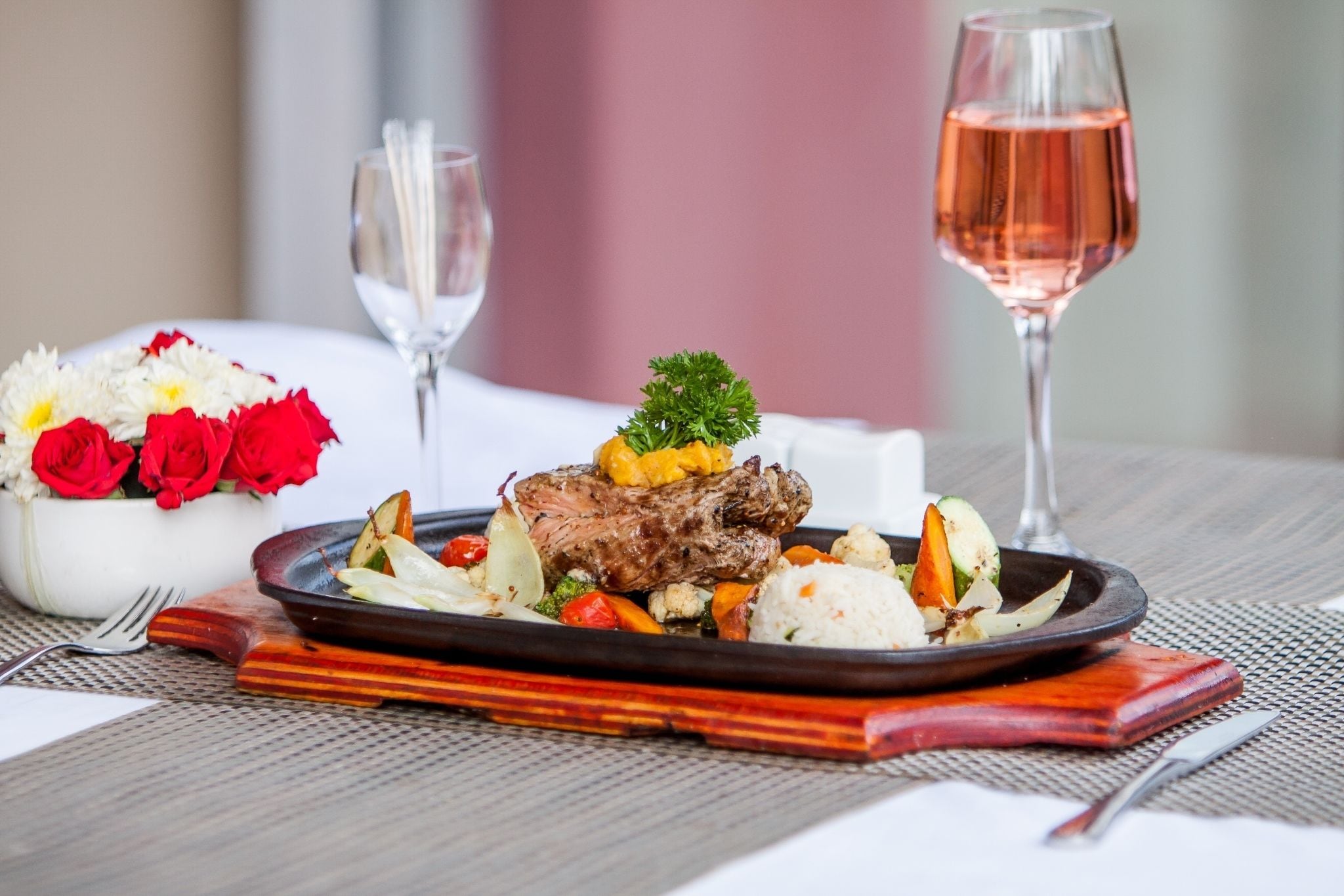 Een eettafel met een bord eten, een glas wijn en een bloemenvaas.
