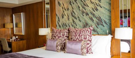 A hotel room with a large bed, wooden paneling, a decorative wall, and a desk with a lamp.