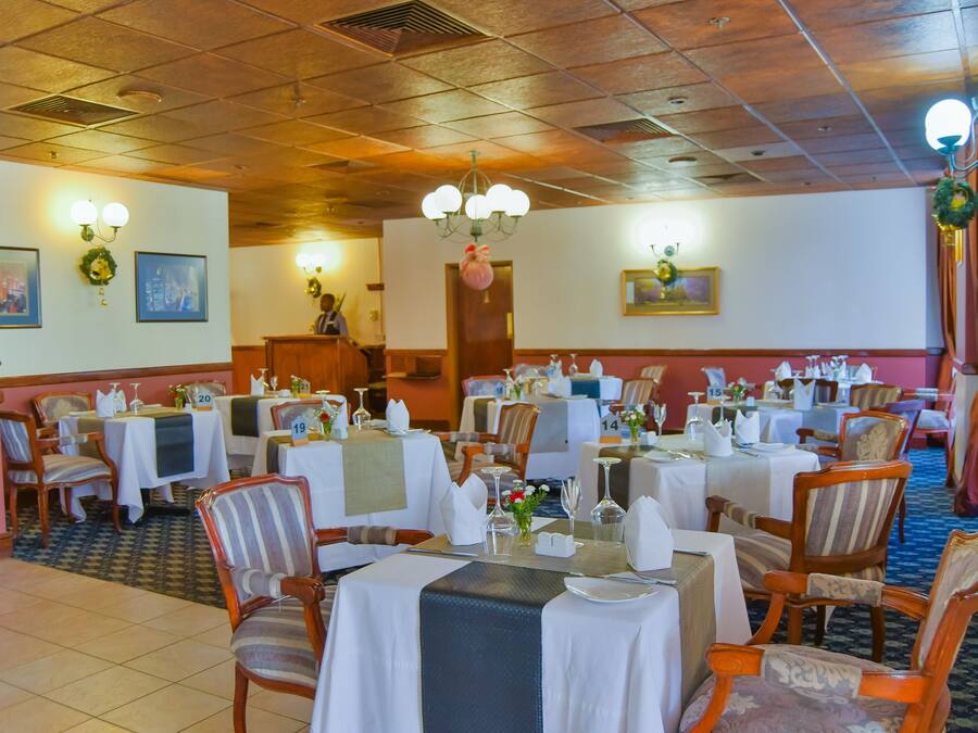 A restaurant with multiple tables set for dining, wooden chairs, and a chandelier.