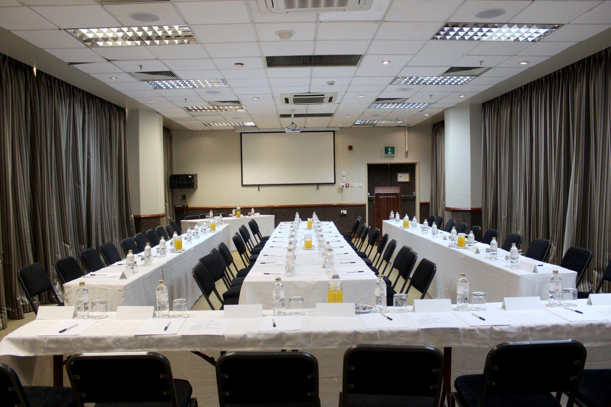 A conference room with a long table, chairs, and a projector screen.