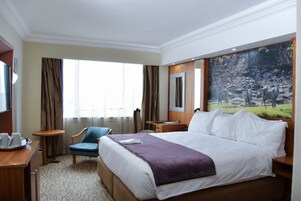 A hotel room with a large bed, a desk, a chair, and a painting of deer on the wall.