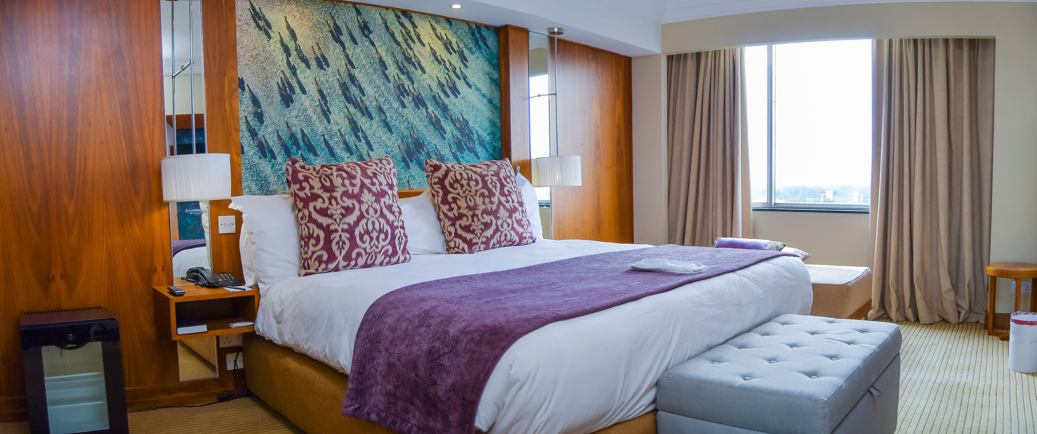 Une chambre d’hôtel avec un grand lit, une table de chevet avec une lampe, une petite table et une fenêtre avec des rideaux.