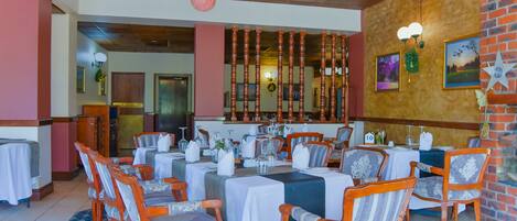 A restaurant with wooden chairs and tables, a brick wall, and a chandelier.