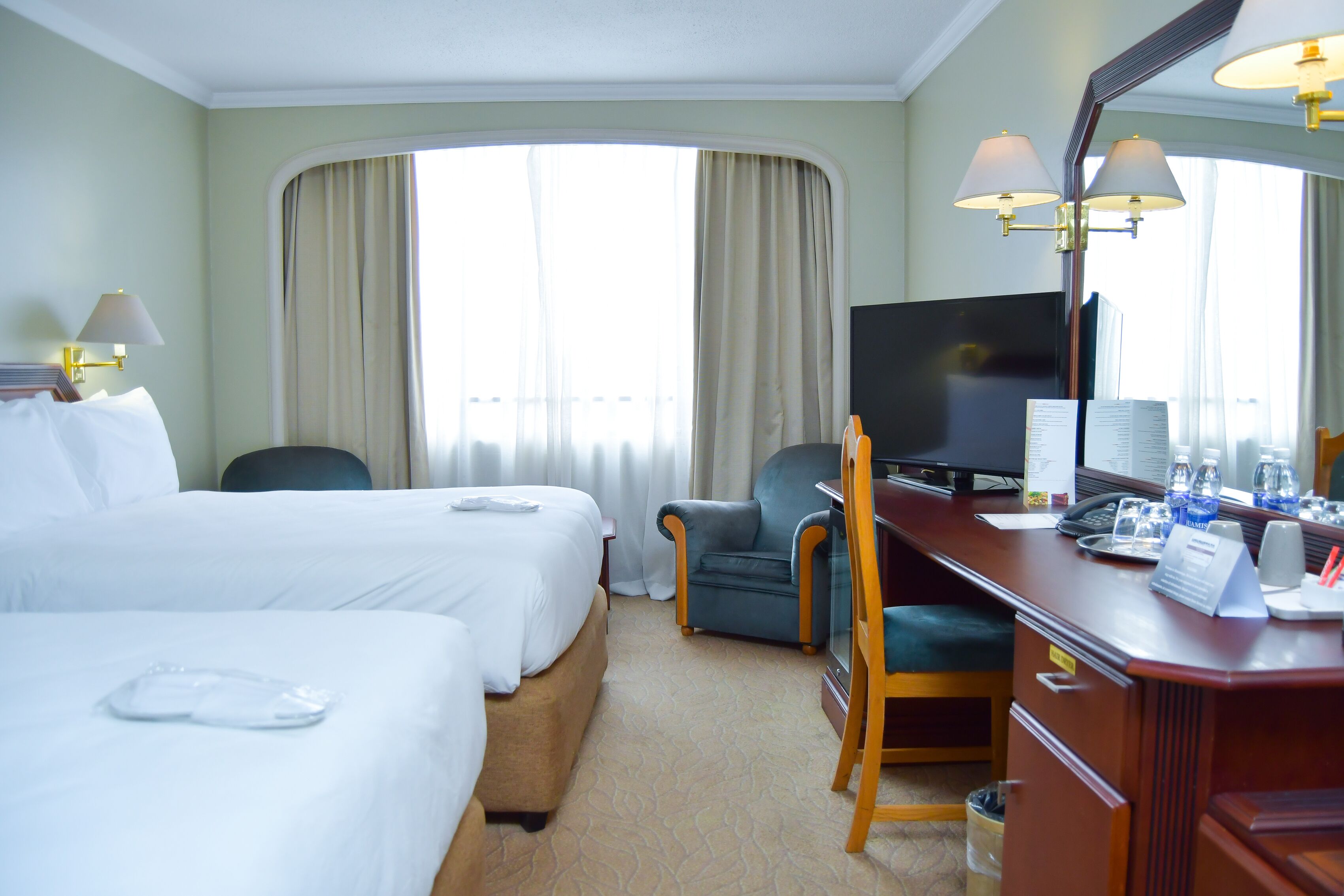 A hotel room with two beds, a desk with a computer, a chair, and a large mirror.