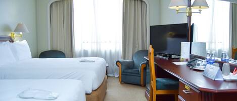 A hotel room with two beds, a desk with a computer, a chair, and a large mirror.