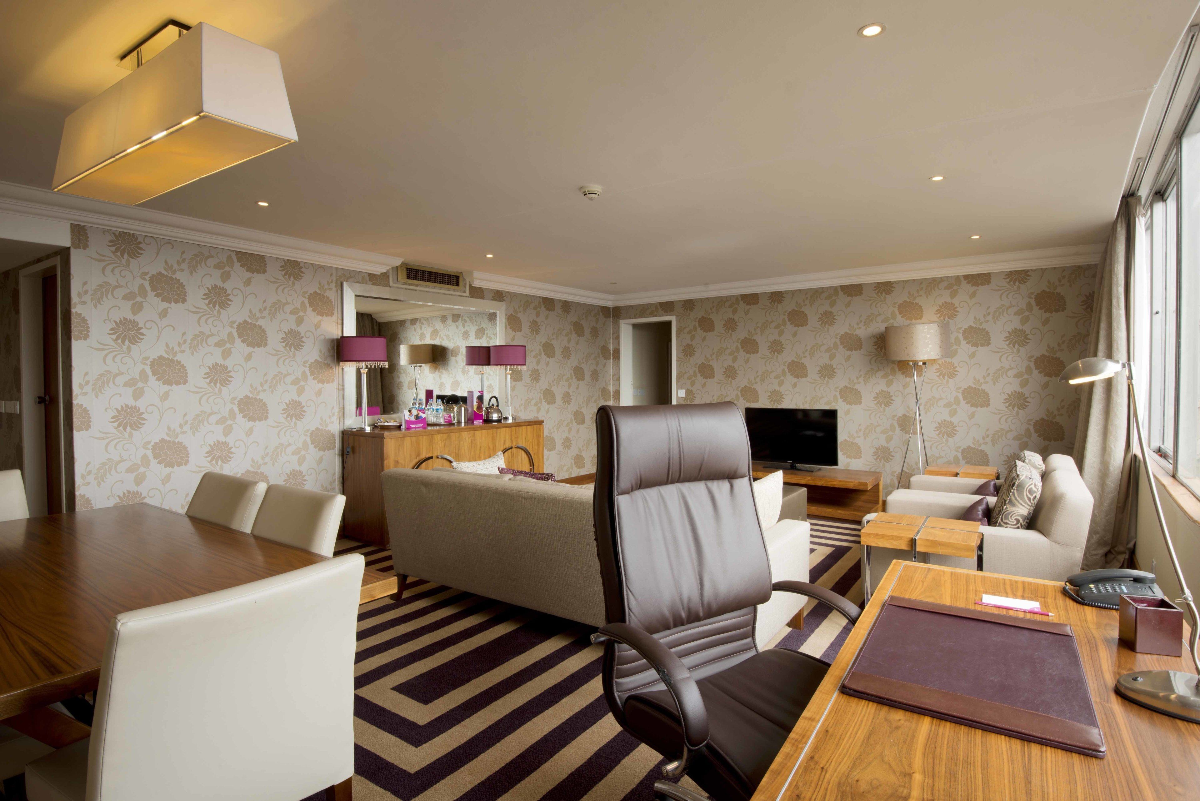 A hotel room with a dining table, a sofa, a desk, and a TV.