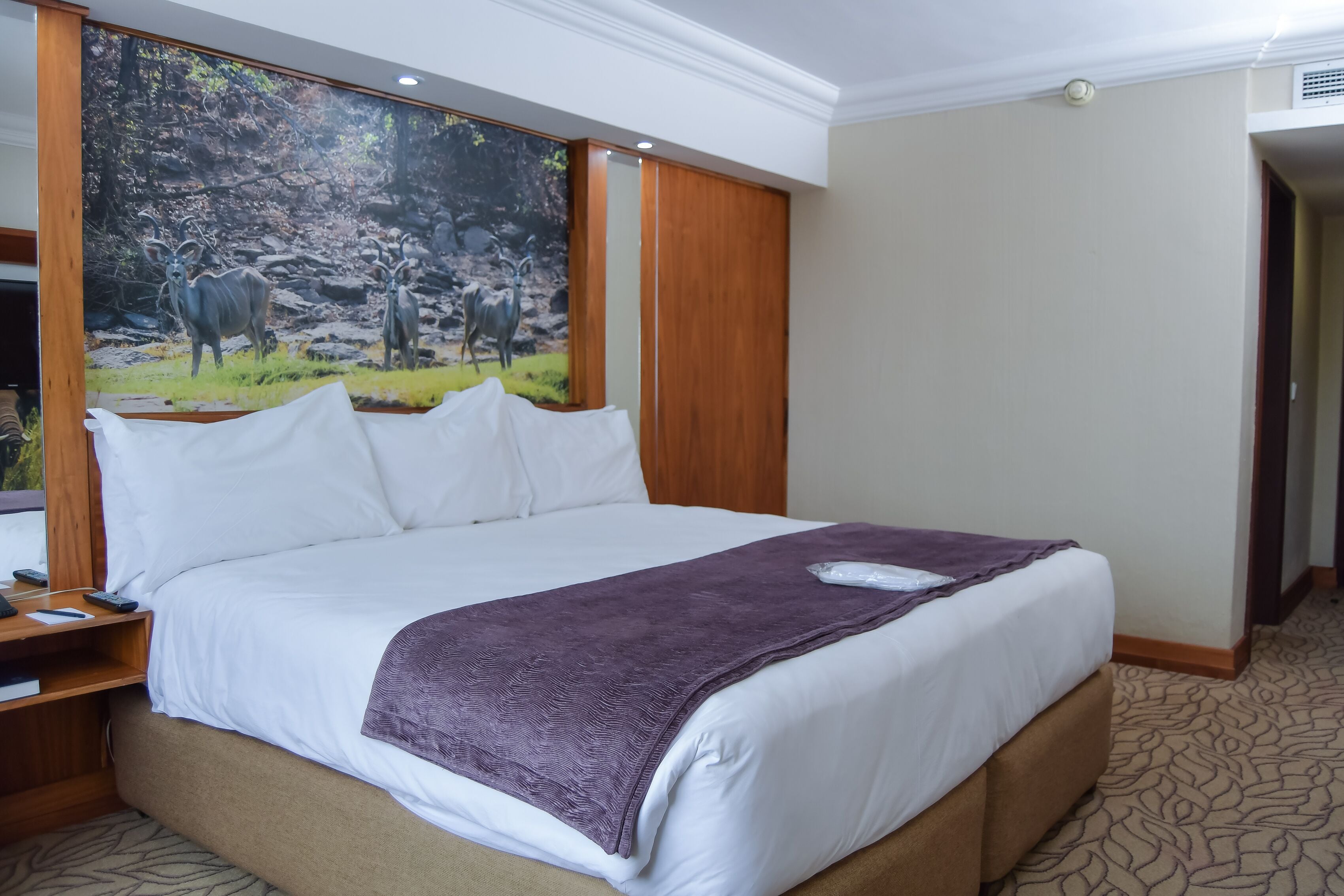 A hotel room with a large bed, white linens, a purple throw blanket, and a painting of deer on the wall.