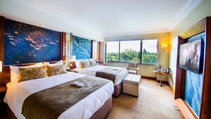 Een hotelkamer met twee bedden, een bureau en een groot raam met uitzicht op de omgeving.