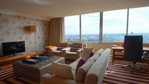 Een hotelkamer met een groot raam, een bank, een stoel, een televisie en een bureau.