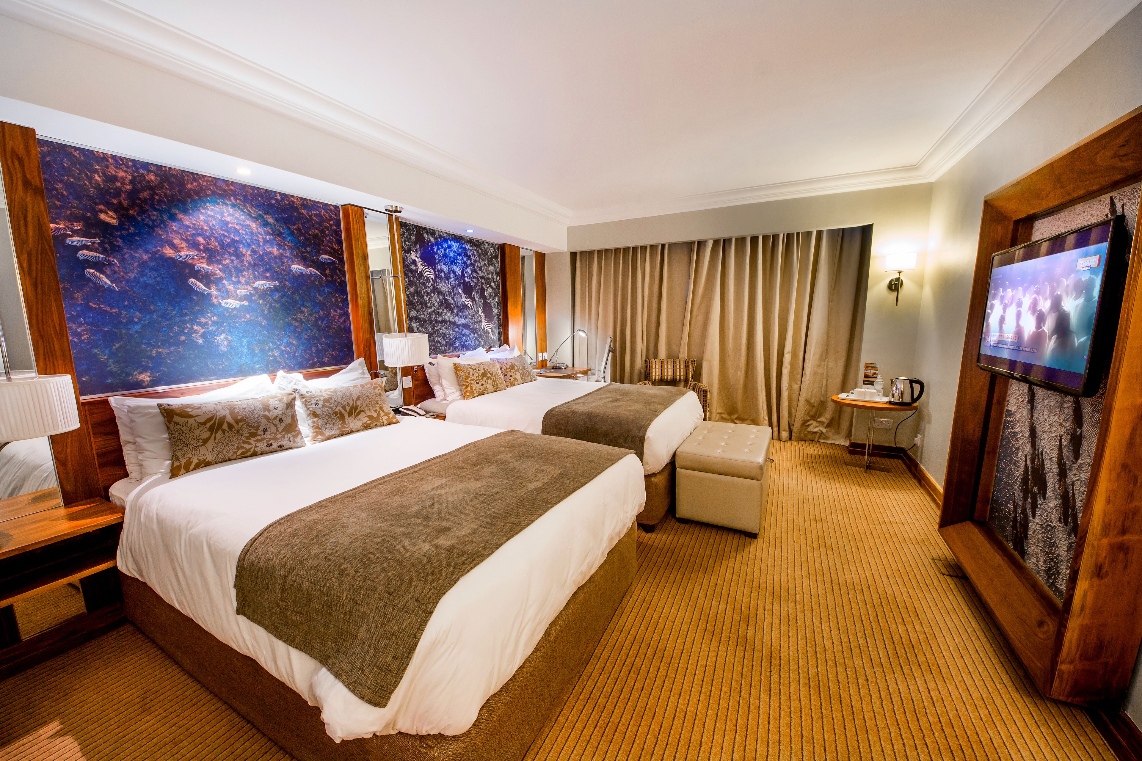 Habitación de hotel con dos camas, televisión, escritorio con lámpara y un cuadro grande en la pared.