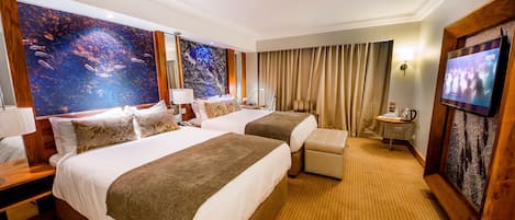 Habitación de hotel con dos camas, televisión, escritorio con lámpara y un cuadro grande en la pared.