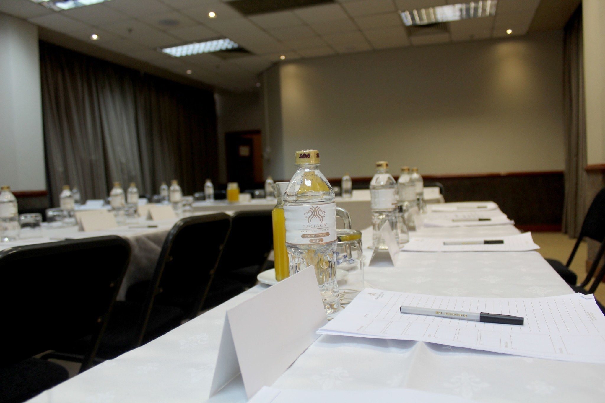 Une salle de conférence avec des tables disposées, sur lesquelles on a placé des porte-noms, des bouteilles d’eau et des documents.