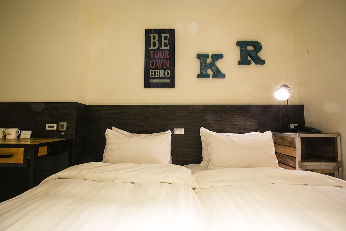 A neatly made bed with white linens, a bedside table with a lamp, and motivational wall art including the letters "K" and "R".