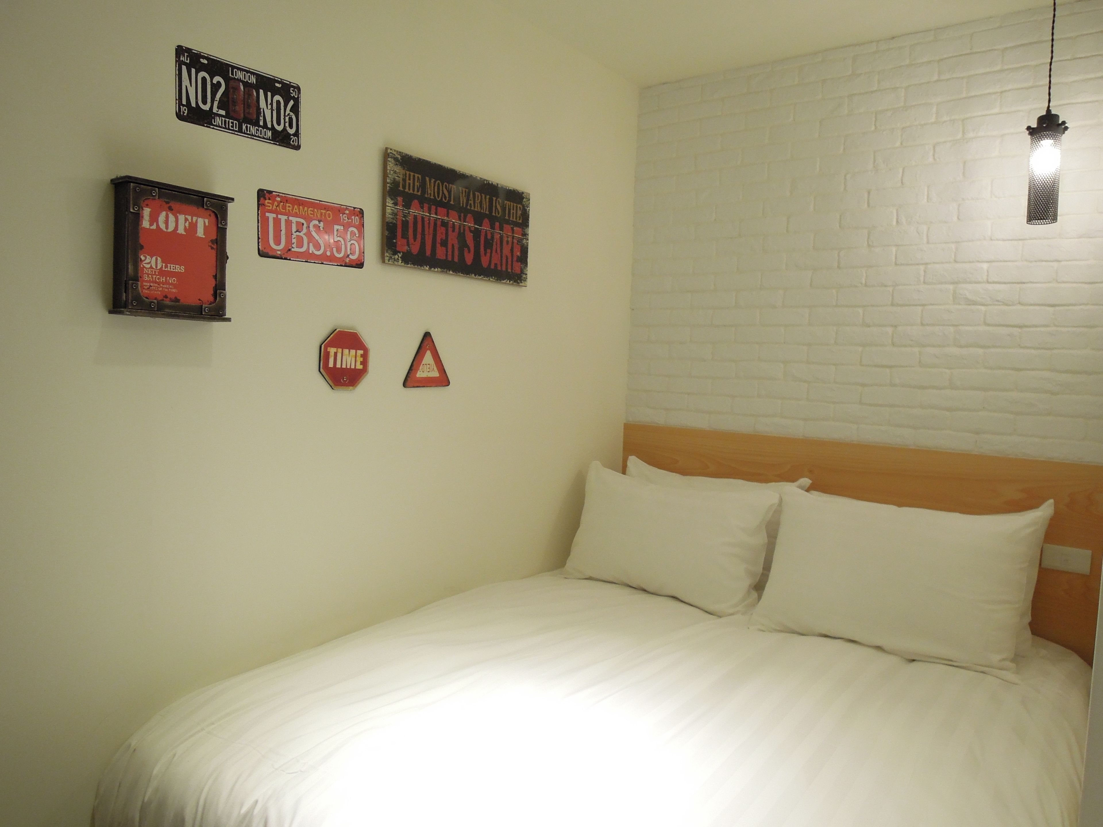 A bedroom with a bed, white bedding, a wooden headboard, and a white brick wall.
