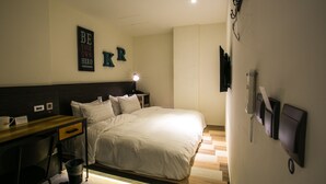 Quarto de hotel com cama, mesa de cabeceira, escrivaninha e cadeira. Há um telefone fixado na parede e um lustre sobre a cama.
