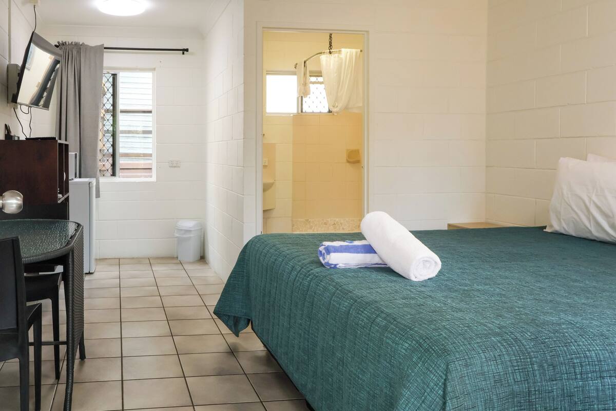 Une chambre d’hôtel avec un lit, un bureau, une chaise, une télévision et une salle de bain visible à travers une porte ouverte.