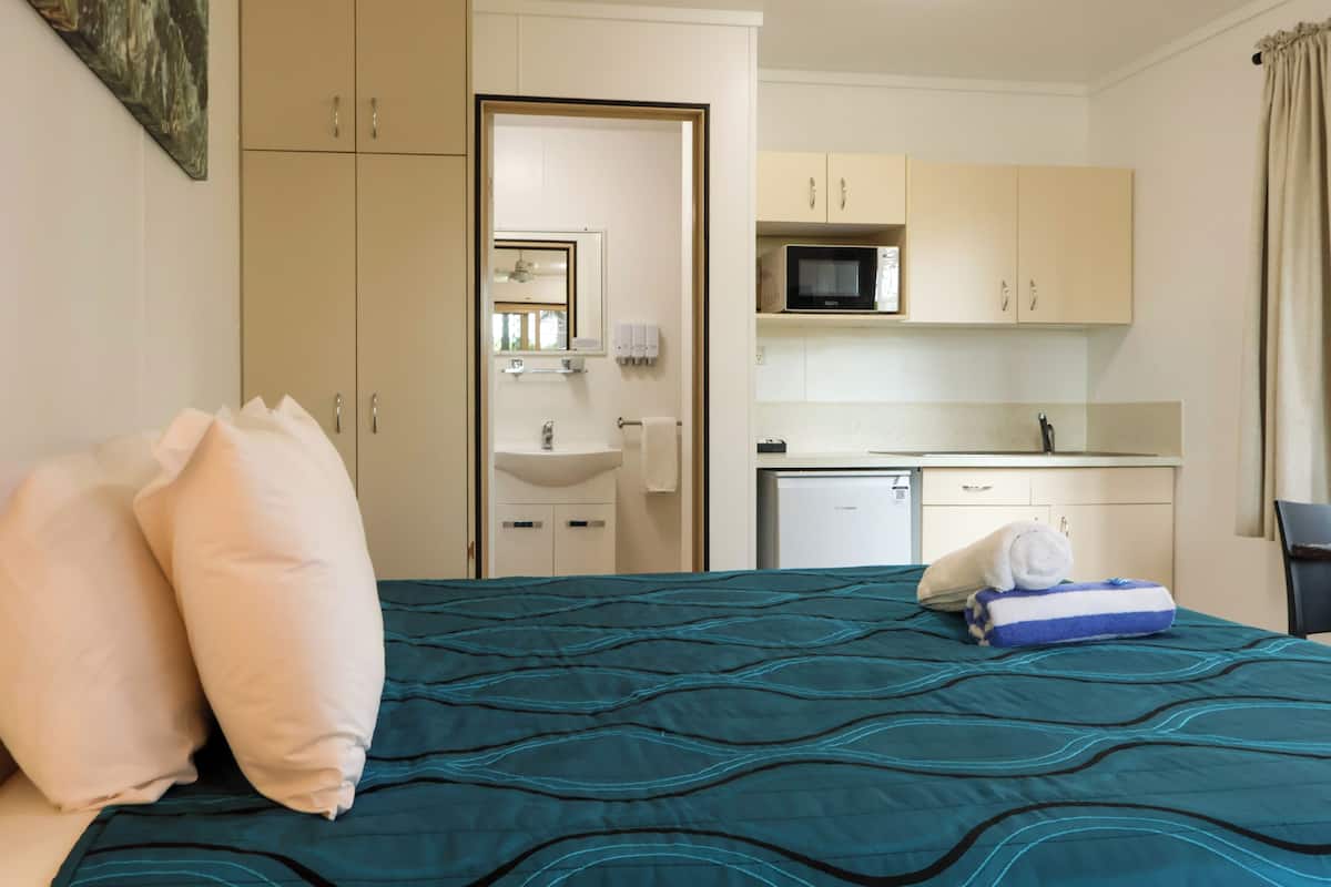 Une chambre d’hôtel comprenant un lit, des oreillers, une couvre-lit à motifs bleus, une petite kitchenette, un four à micro-ondes et un évier.
