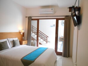 A hotel room with a bed, a nightstand, an air conditioning unit, a TV mounted on the wall, and a staircase leading to an outdoor area. - Spunky Premiere Kuta (Keroboken Kelod)