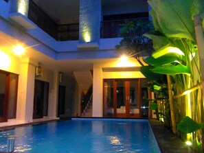 An indoor swimming pool with a glass enclosure, surrounded by a building with a modern design, including a staircase and large windows. - Spunky Premiere Kuta (Keroboken Kelod)