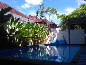 A swimming pool with a clear blue water surface reflecting the surrounding buildings and trees. - Spunky Premiere Kuta (Keroboken Kelod)