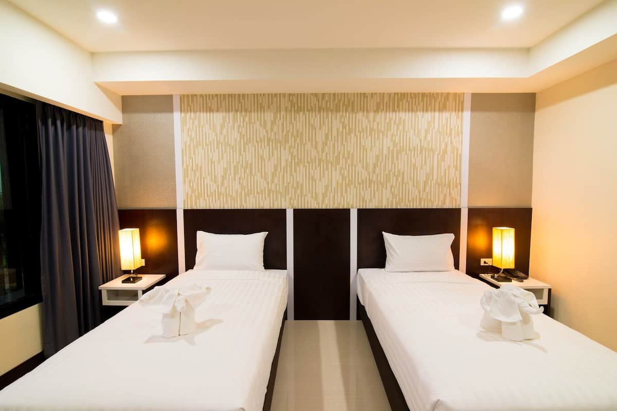 A hotel room with two beds, a large window with curtains, and a decorative wall panel.