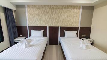 Habitación de hotel con dos camas individuales, un ventanal con cortinas, un panel en la pared y una mesita de noche con teléfono.