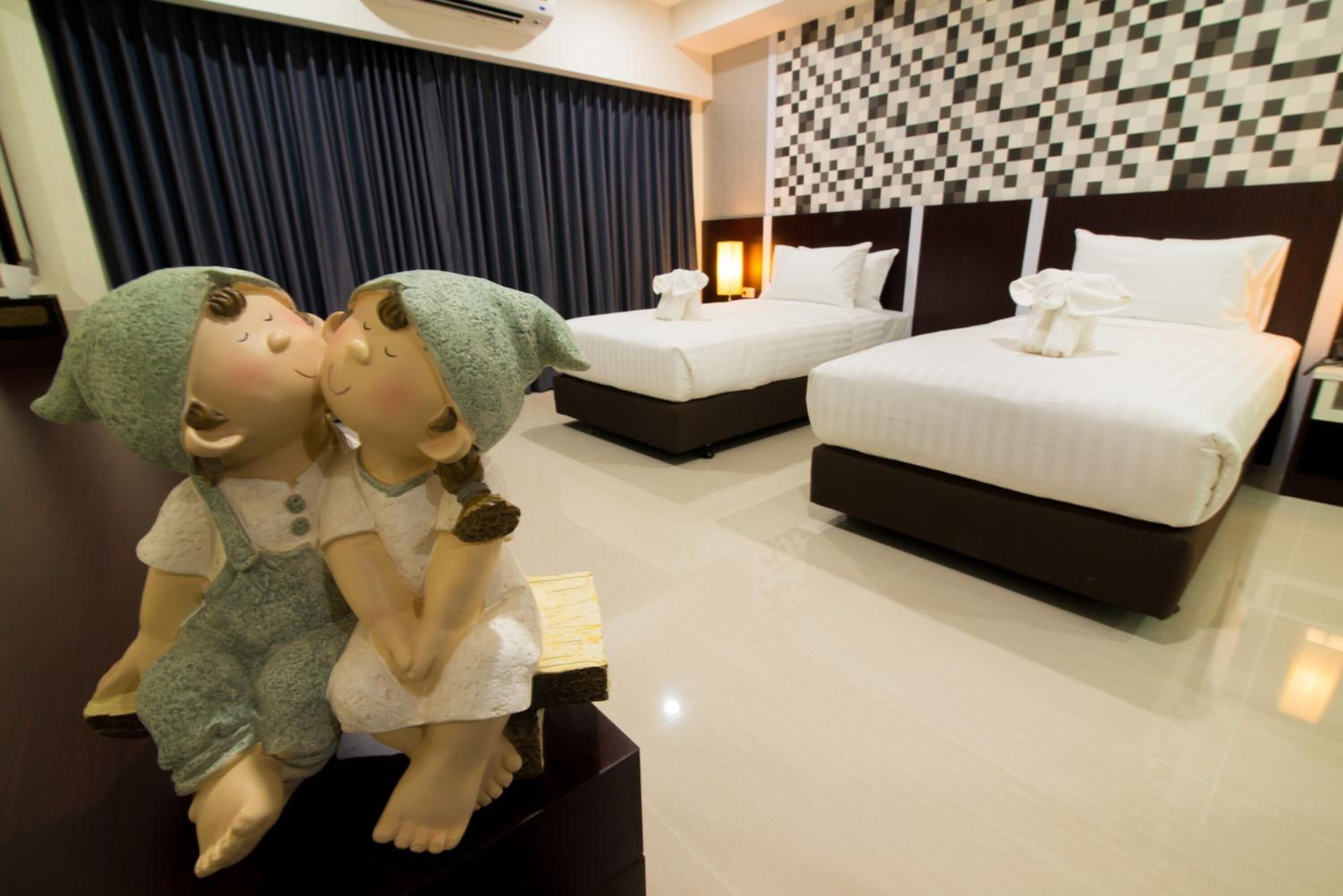 Quarto de hotel com duas camas, cabeceira xadrez e uma estátua decorativa de duas figuras sobre uma mesa.